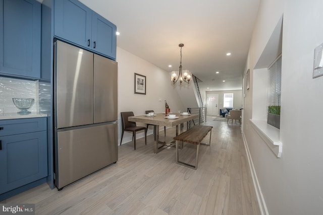 kitchen featuring pendant lighting, light hardwood / wood-style floors, stainless steel refrigerator, blue cabinets, and a chandelier