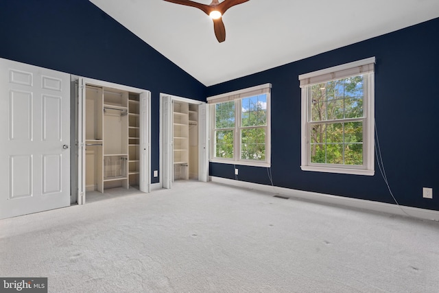 unfurnished bedroom with ceiling fan, light colored carpet, high vaulted ceiling, and multiple closets