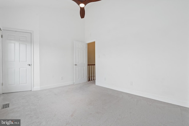 carpeted empty room featuring ceiling fan and a high ceiling