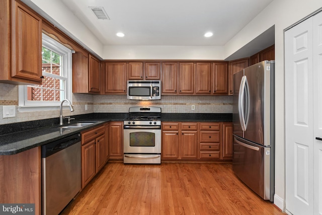 kitchen featuring appliances with stainless steel finishes, dark stone counters, decorative backsplash, sink, and light hardwood / wood-style flooring