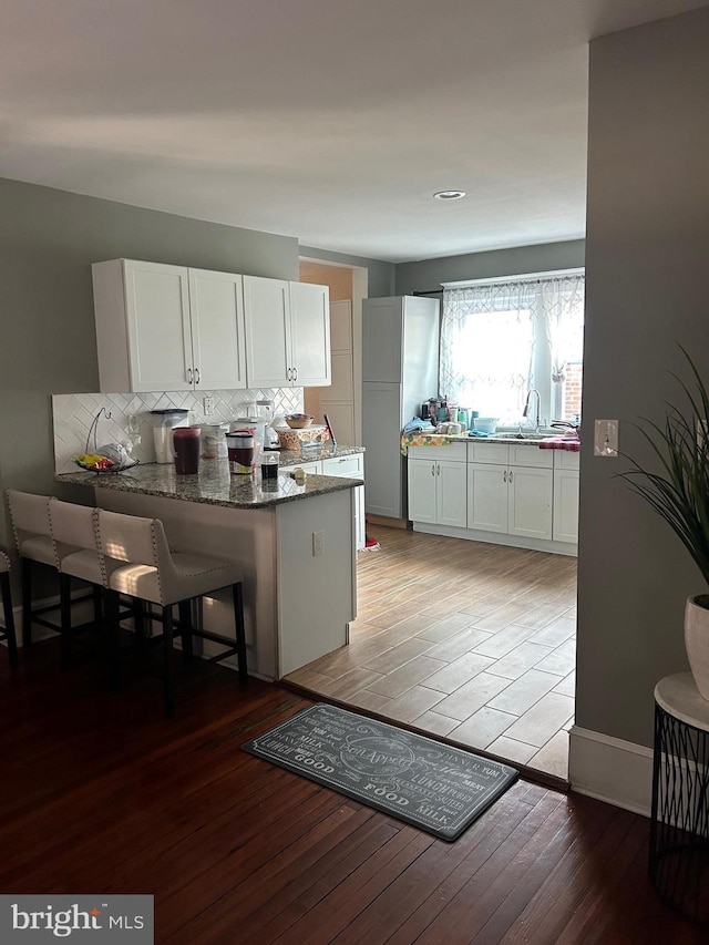 kitchen featuring white cabinets, dark stone counters, a kitchen breakfast bar, kitchen peninsula, and light wood-type flooring