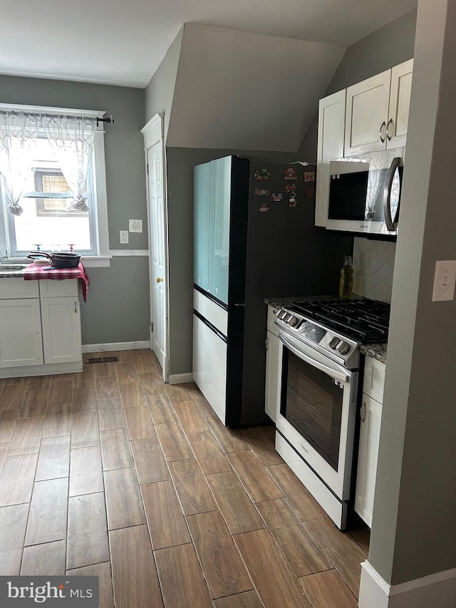 kitchen with white cabinetry, stainless steel appliances, decorative backsplash, lofted ceiling, and dark stone counters