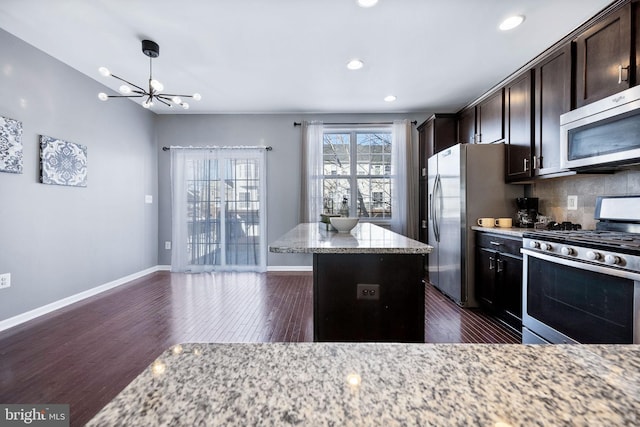 kitchen featuring dark hardwood / wood-style flooring, appliances with stainless steel finishes, light stone countertops, a kitchen island, and decorative backsplash