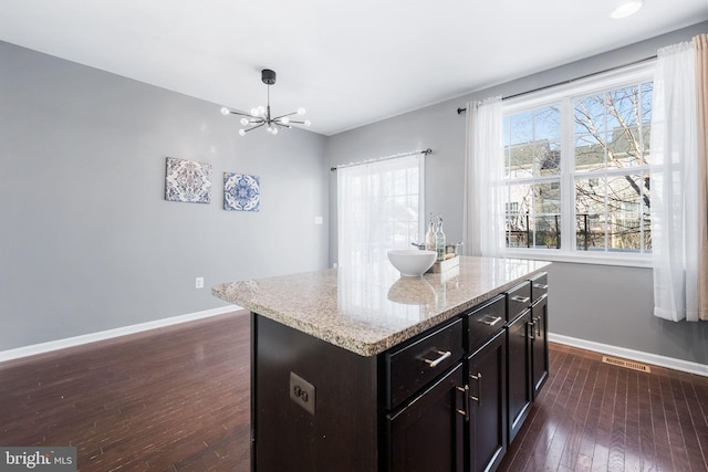 kitchen featuring dark wood-type flooring, light stone countertops, a center island, a chandelier, and dark brown cabinetry