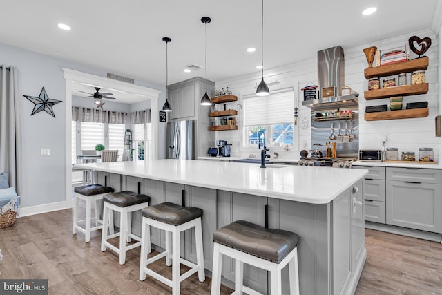 kitchen with ceiling fan, gray cabinetry, wall chimney range hood, light hardwood / wood-style flooring, and a center island