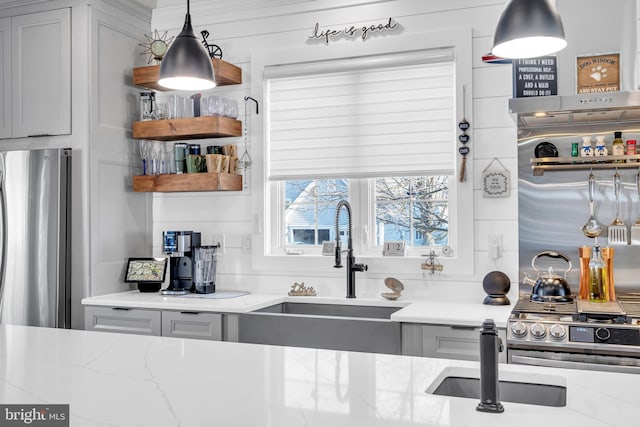 kitchen featuring gray cabinets, sink, hanging light fixtures, stainless steel fridge, and light stone counters