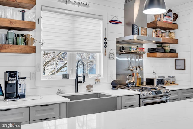 kitchen with extractor fan, sink, gray cabinets, light stone counters, and stainless steel range with gas cooktop