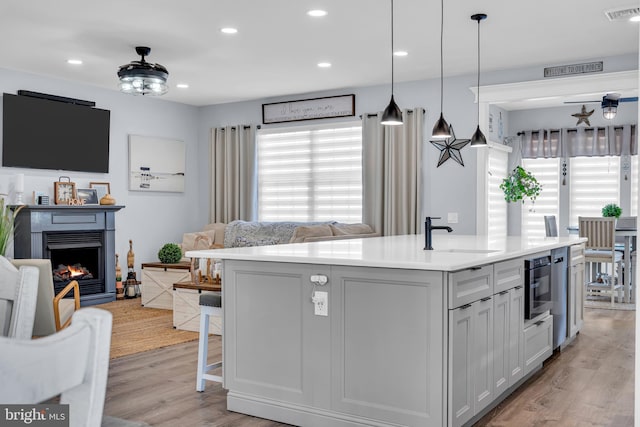 kitchen featuring sink, pendant lighting, a center island with sink, and light wood-type flooring