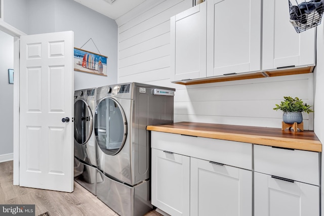 laundry room featuring washing machine and dryer, cabinets, wooden walls, and light wood-type flooring