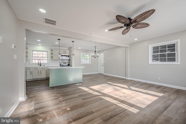 unfurnished living room featuring ceiling fan with notable chandelier, sink, hardwood / wood-style floors, and a healthy amount of sunlight