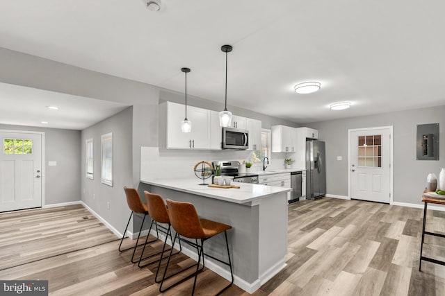 kitchen with a kitchen bar, kitchen peninsula, stainless steel appliances, decorative light fixtures, and white cabinets