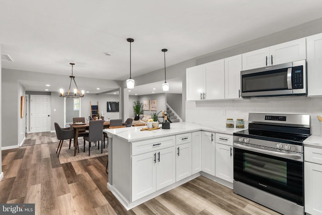 kitchen with appliances with stainless steel finishes, white cabinets, kitchen peninsula, and hanging light fixtures