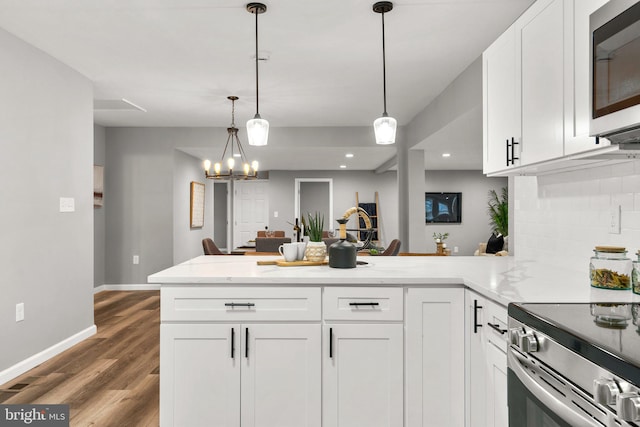 kitchen featuring kitchen peninsula, decorative backsplash, white cabinetry, hanging light fixtures, and appliances with stainless steel finishes