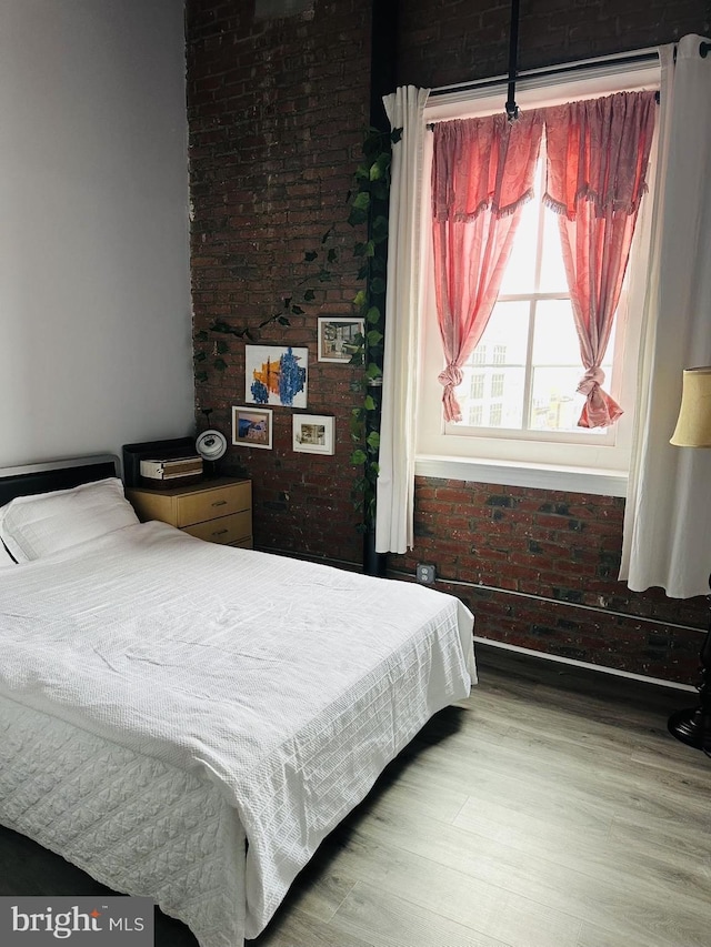 bedroom featuring brick wall and wood-type flooring