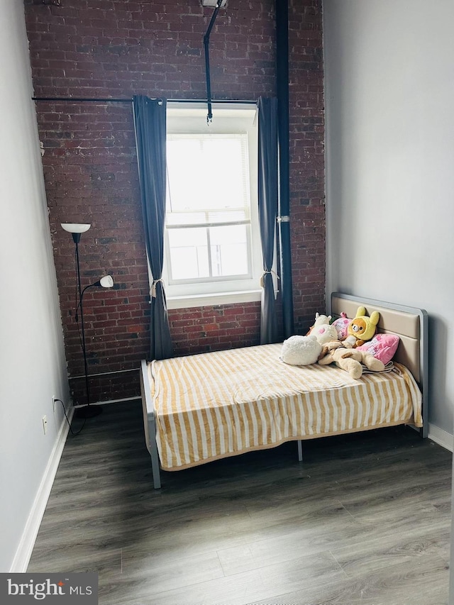 unfurnished bedroom featuring hardwood / wood-style flooring and brick wall