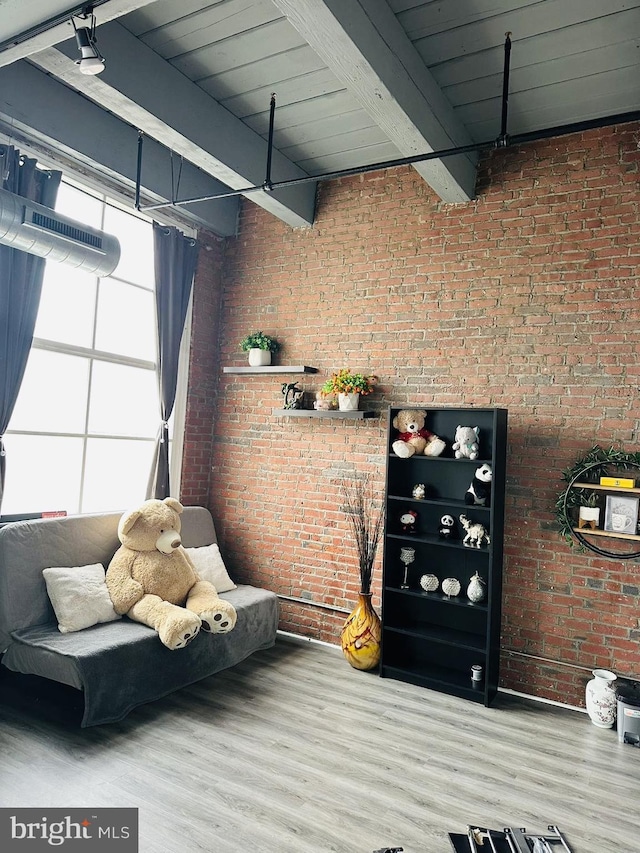 living area featuring beam ceiling, wood-type flooring, and brick wall