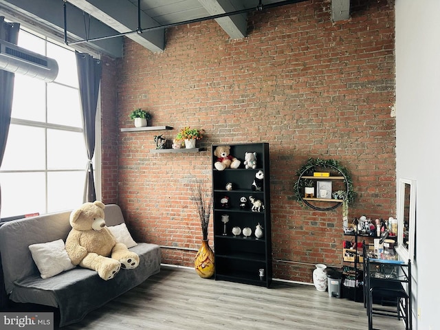 living area featuring beamed ceiling, brick wall, a towering ceiling, and hardwood / wood-style floors