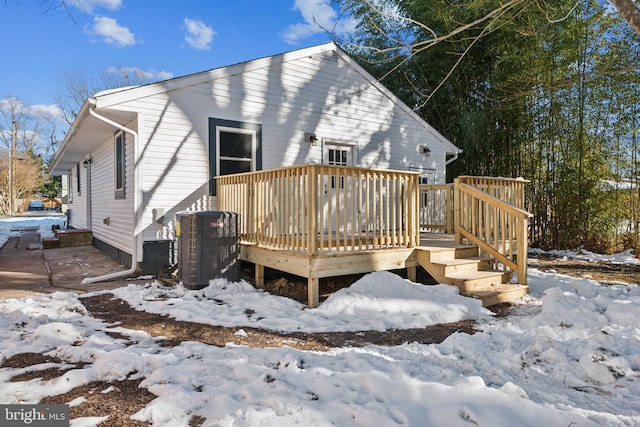 snow covered back of property featuring central AC and a wooden deck