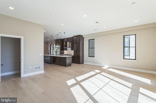 interior space with pendant lighting, light hardwood / wood-style floors, a center island, dark brown cabinets, and wall chimney exhaust hood