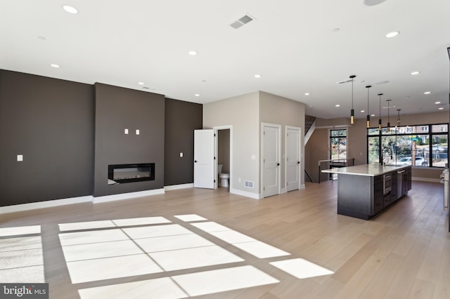 kitchen featuring decorative light fixtures, light hardwood / wood-style flooring, dark brown cabinets, and an island with sink