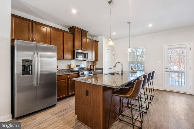 kitchen with appliances with stainless steel finishes, sink, dark stone countertops, decorative light fixtures, and an island with sink