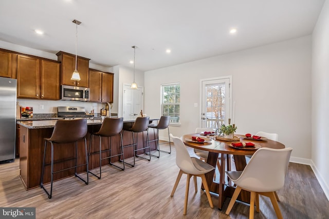 kitchen featuring pendant lighting, appliances with stainless steel finishes, light wood-type flooring, a center island with sink, and a breakfast bar area