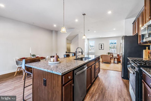 kitchen with appliances with stainless steel finishes, hanging light fixtures, a kitchen breakfast bar, sink, and an island with sink