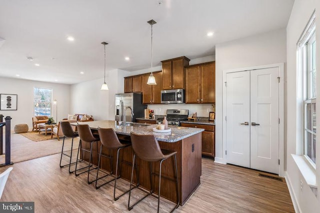 kitchen with a kitchen breakfast bar, light hardwood / wood-style flooring, appliances with stainless steel finishes, light stone countertops, and a center island with sink