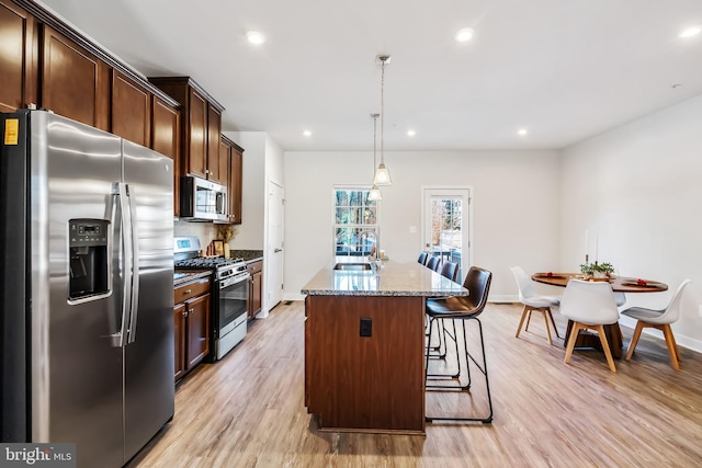 kitchen with stone counters, hanging light fixtures, sink, an island with sink, and stainless steel appliances