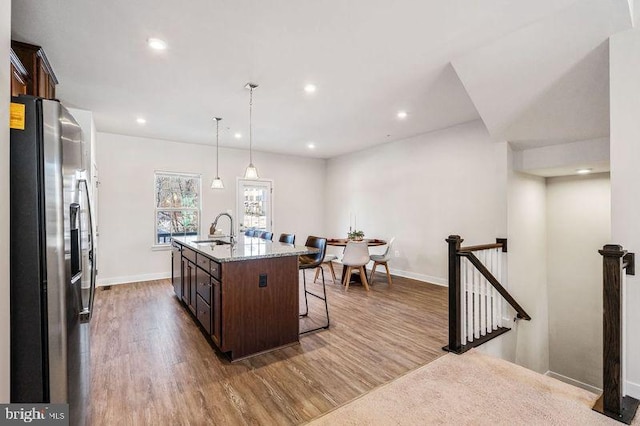 kitchen featuring appliances with stainless steel finishes, a kitchen island with sink, sink, decorative light fixtures, and a breakfast bar