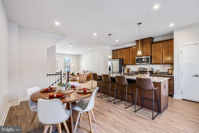 kitchen with pendant lighting, light stone countertops, an island with sink, light hardwood / wood-style floors, and stainless steel appliances