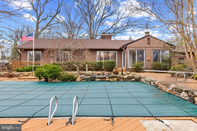 rear view of house featuring a deck, a patio area, a covered pool, and a chimney