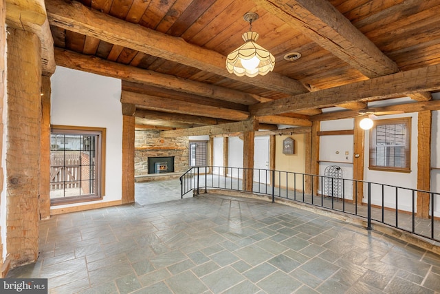 unfurnished living room featuring a stone fireplace, beamed ceiling, stone tile flooring, and wood ceiling