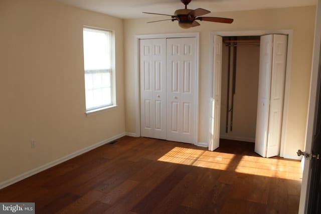 unfurnished bedroom featuring dark wood-type flooring, ceiling fan, multiple closets, and multiple windows