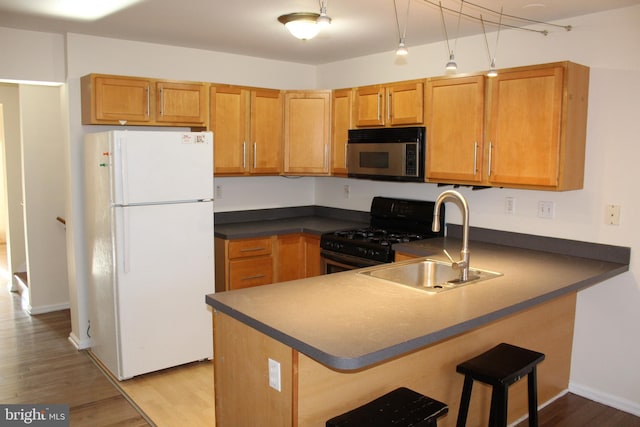 kitchen featuring white refrigerator, black gas range oven, sink, kitchen peninsula, and light hardwood / wood-style flooring