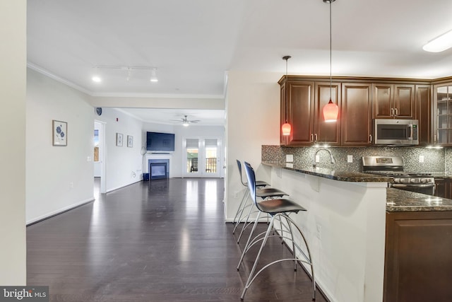 kitchen with a breakfast bar area, decorative light fixtures, dark stone countertops, kitchen peninsula, and stainless steel appliances