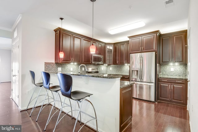 kitchen with hanging light fixtures, dark stone countertops, appliances with stainless steel finishes, a kitchen breakfast bar, and kitchen peninsula