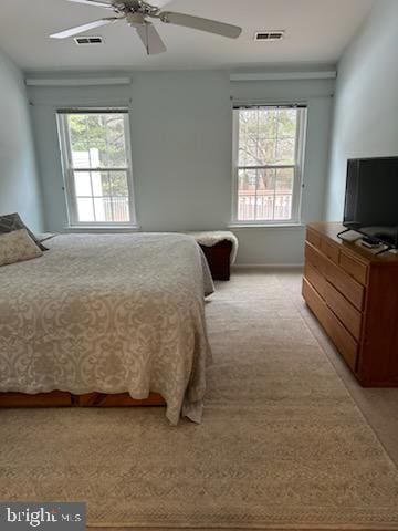 bedroom with ceiling fan, light colored carpet, and multiple windows