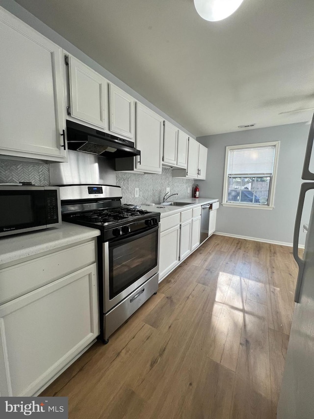 kitchen with appliances with stainless steel finishes, white cabinetry, sink, decorative backsplash, and light hardwood / wood-style flooring