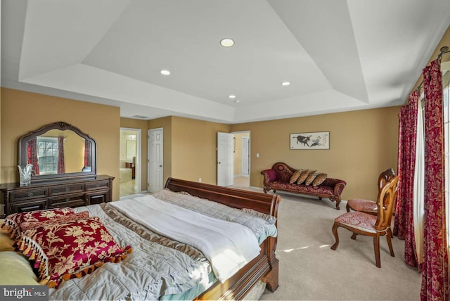 bedroom with ensuite bathroom, light carpet, and a raised ceiling