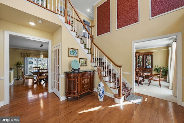 stairs featuring crown molding, a towering ceiling, and wood-type flooring