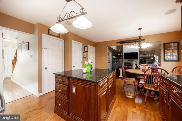 kitchen with dark stone countertops, hanging light fixtures, light hardwood / wood-style flooring, and an inviting chandelier