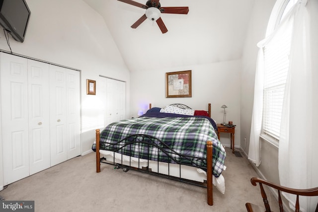 bedroom featuring ceiling fan, two closets, light colored carpet, and high vaulted ceiling