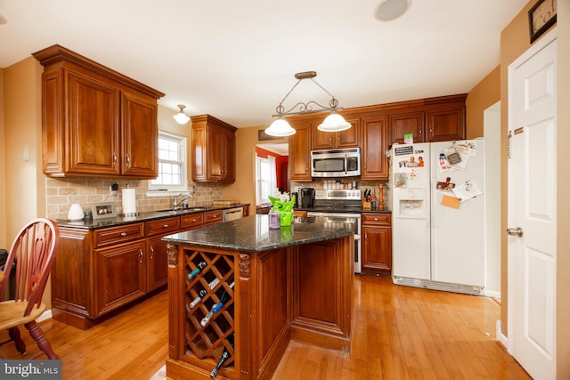 kitchen featuring appliances with stainless steel finishes, pendant lighting, sink, dark stone countertops, and a center island