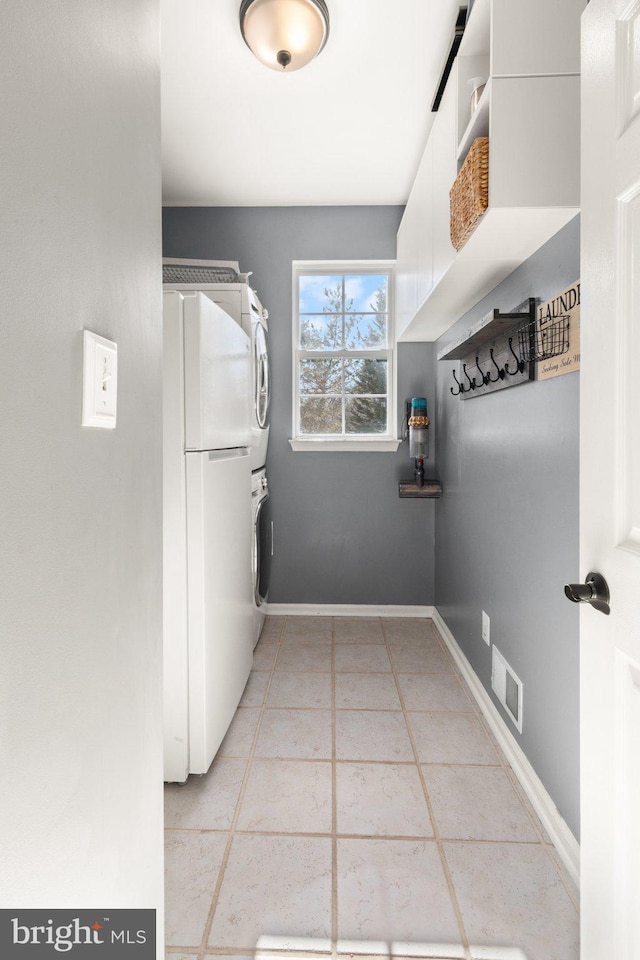 laundry area featuring cabinets, stacked washer and clothes dryer, and light tile patterned floors