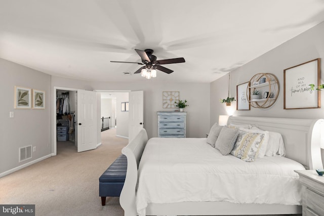 bedroom with a walk in closet, light carpet, and ceiling fan