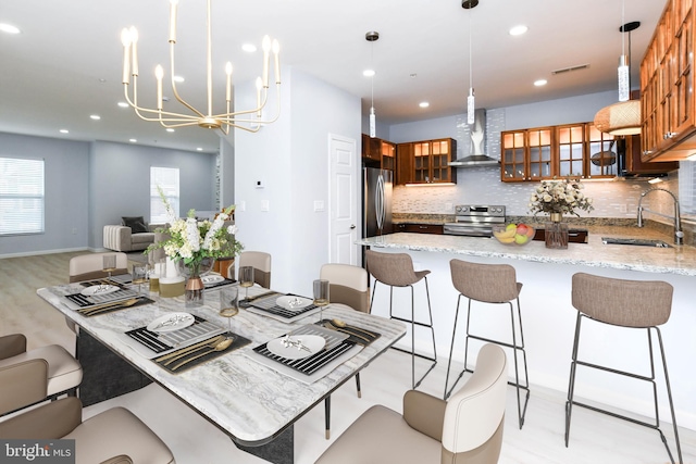 kitchen featuring backsplash, wall chimney range hood, sink, hanging light fixtures, and light stone countertops