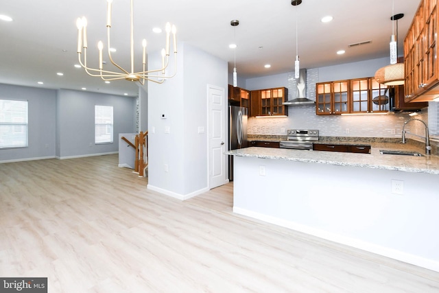 kitchen with pendant lighting, sink, wall chimney range hood, and light stone counters