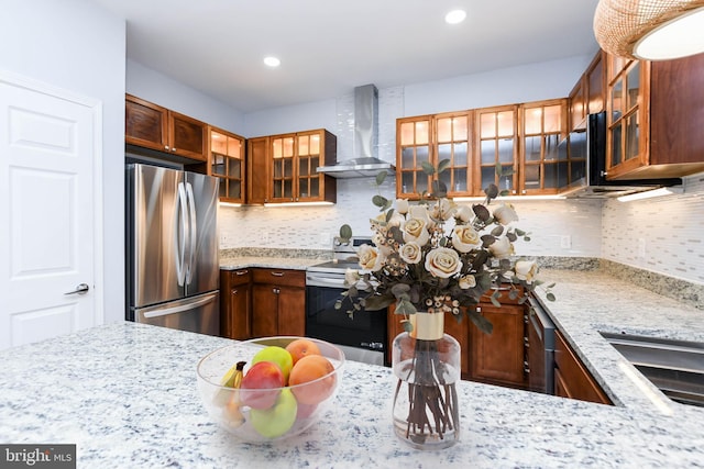 kitchen with tasteful backsplash, light stone countertops, wall chimney exhaust hood, and stainless steel appliances