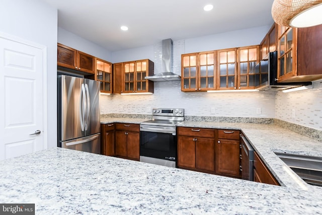 kitchen featuring decorative backsplash, light stone counters, appliances with stainless steel finishes, and wall chimney exhaust hood